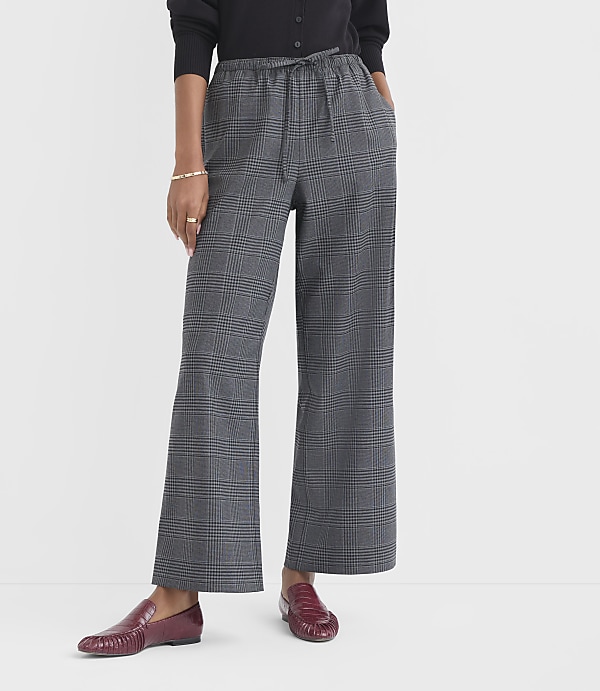 A person in plaid wide-leg pants and burgundy loafers stands against a plain white background.