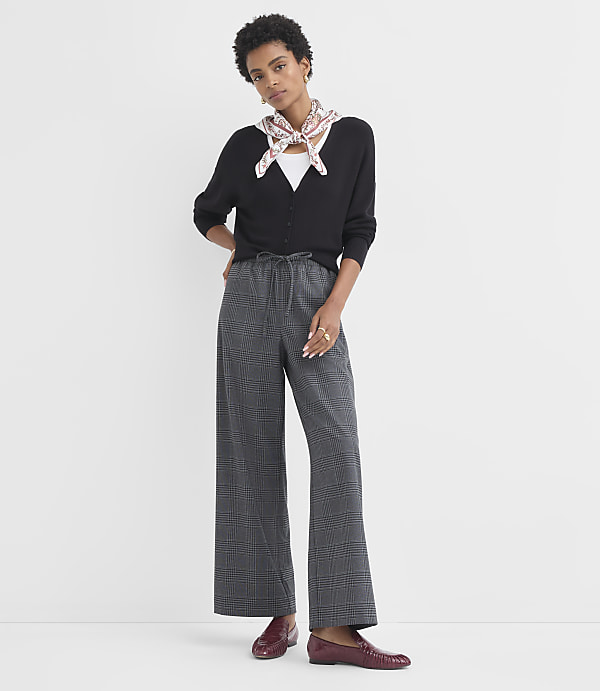 A woman in a black cardigan and plaid pants stands against a plain white background.