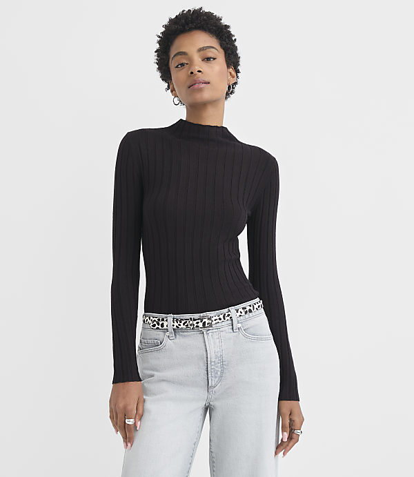 A woman in a black ribbed turtleneck and light wash jeans stands against a plain white background.