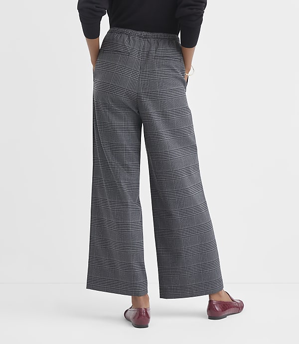 A person wearing plaid wide-leg pants and red loafers stands against a plain white background.