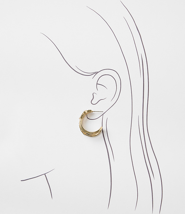 A gold hoop earring with textured detailing is worn on a sketched ear against a white background.