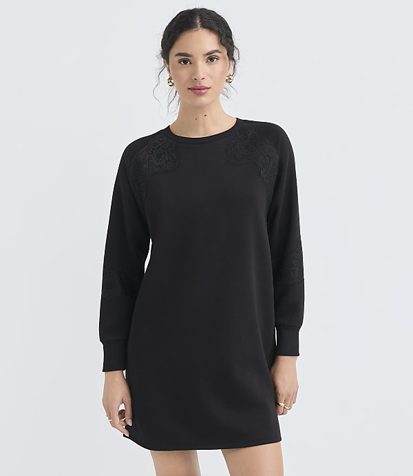 A woman in a black dress stands against a plain white background.