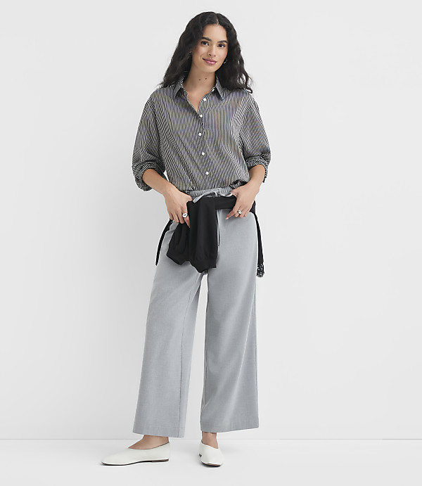 A woman in a striped shirt and wide-leg pants stands against a plain white background.