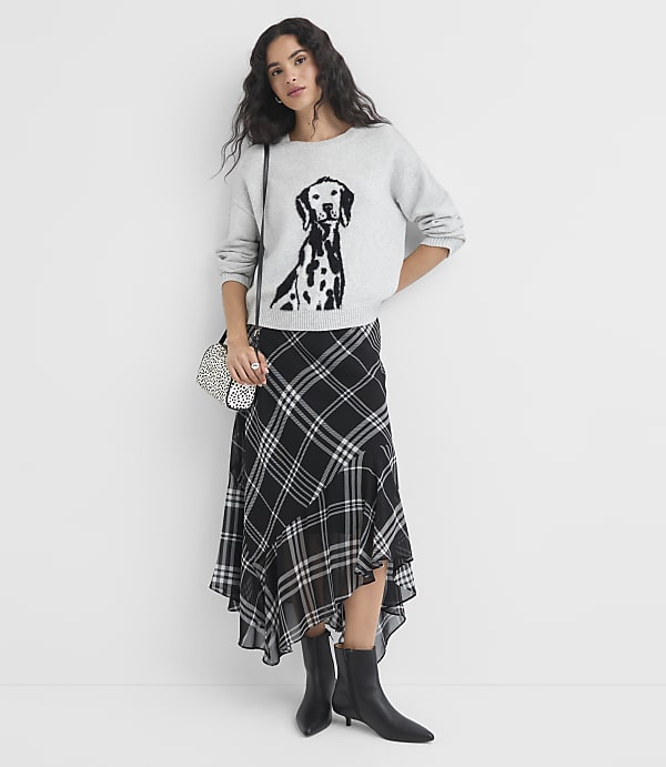 A woman in a Dalmatian-print sweatshirt and plaid skirt stands against a plain white background.