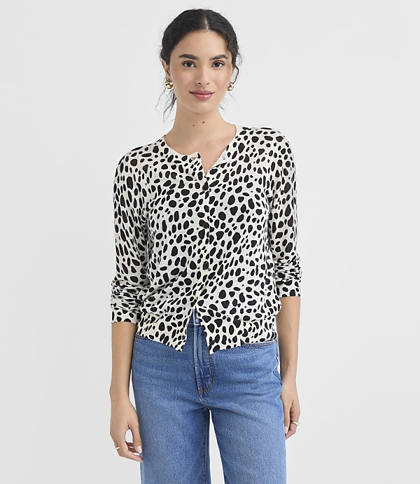 A woman in a dalmatian-print cardigan and blue jeans stands against a plain white background.