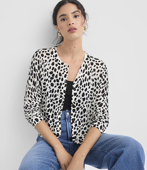 A woman in a dalmatian-print cardigan and blue jeans sits against a plain white background.