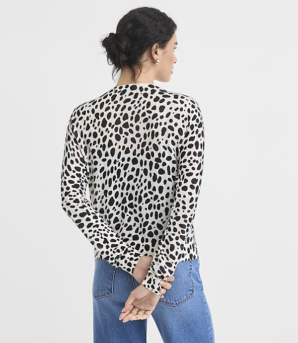 A woman in a dalmatian-print sweater and blue jeans stands with her back to the camera against a plain white background.