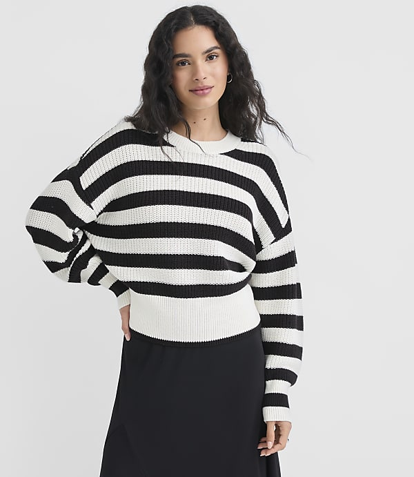 A woman in a black and white striped sweater stands against a plain white background.