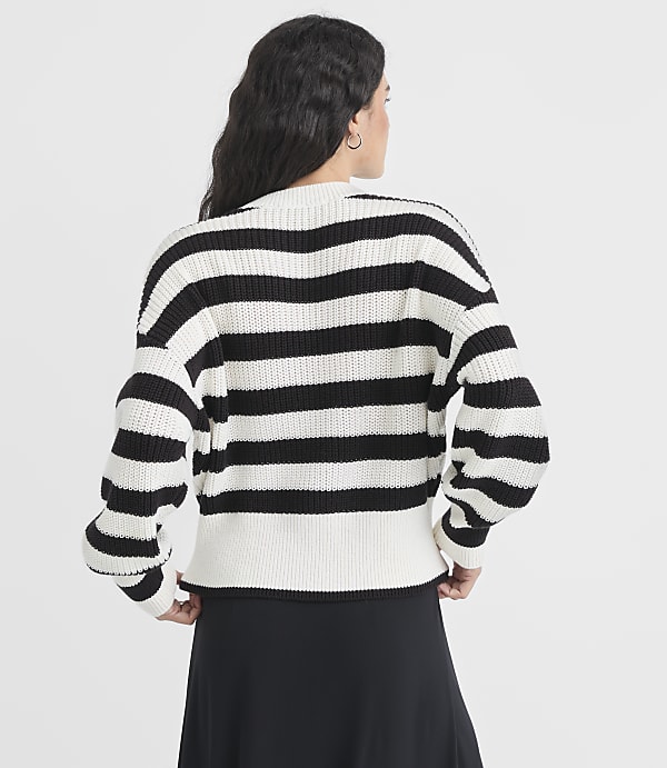 A woman in a black and white striped sweater stands against a plain white background.