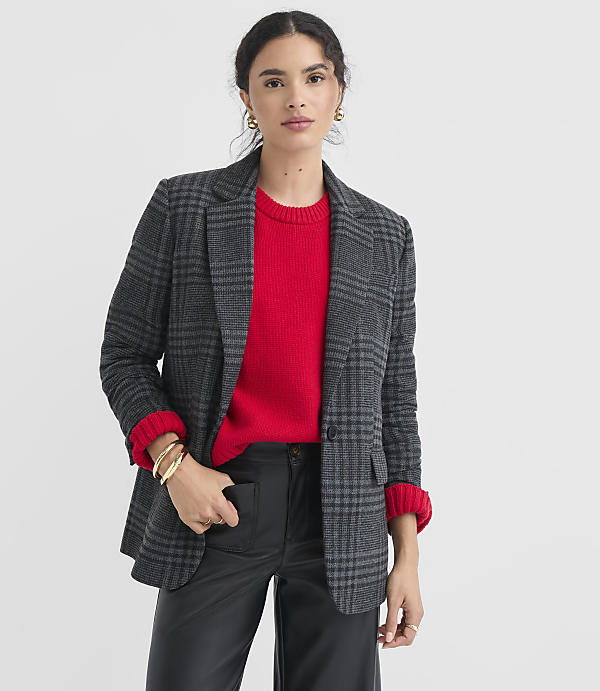 A woman in a red sweater and plaid blazer stands against a plain white background.