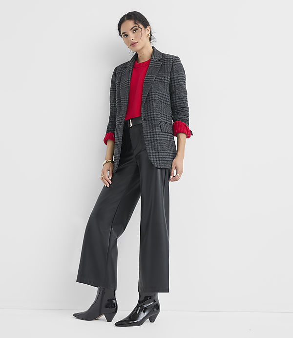 A woman in a plaid blazer, red sweater, and black leather pants stands against a plain white background.