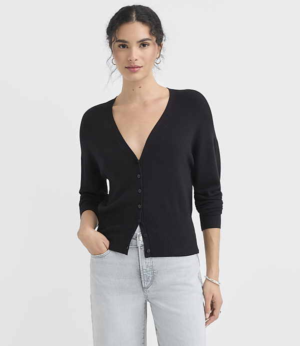 A woman in a black cardigan and light blue jeans stands against a plain white background.