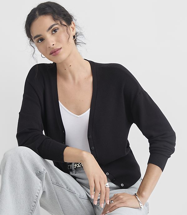 A woman in a black cardigan and white top poses against a plain white background.