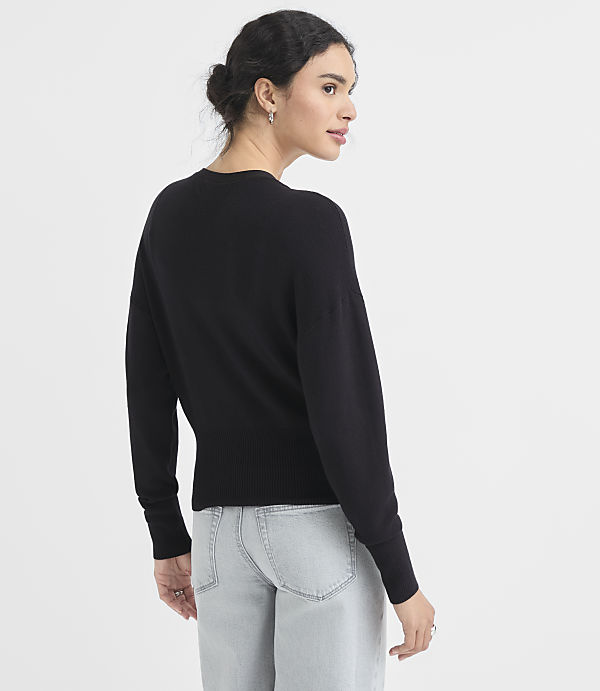 A woman in a black sweater and light-wash jeans stands against a plain white background.