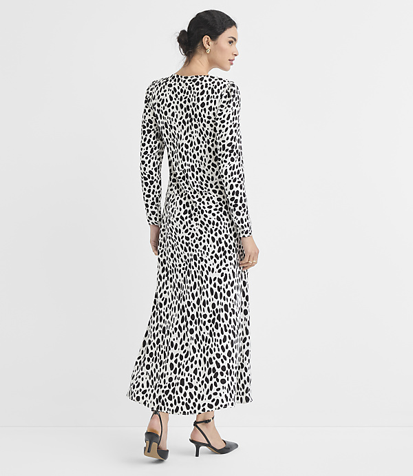 A woman in a black and white dalmatian print dress stands against a plain white background.