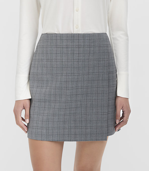 A woman in a white shirt models a grey plaid mini skirt against a plain white background.