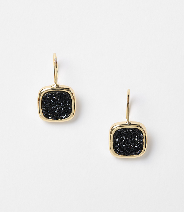 A pair of gold-framed, square black druzy earrings hang against a plain white background.