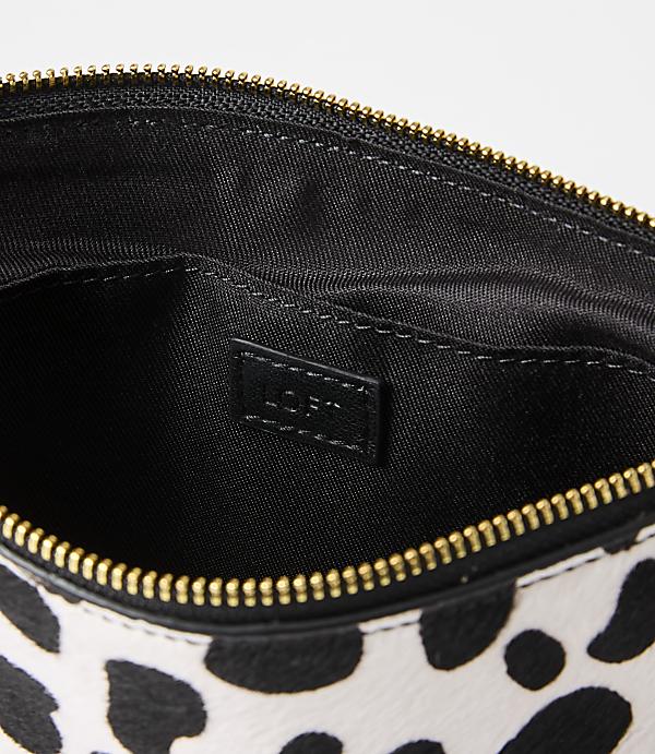 A black and white spotted clutch with a gold zipper is open to reveal its black interior, which has a "LOFT" logo tag.