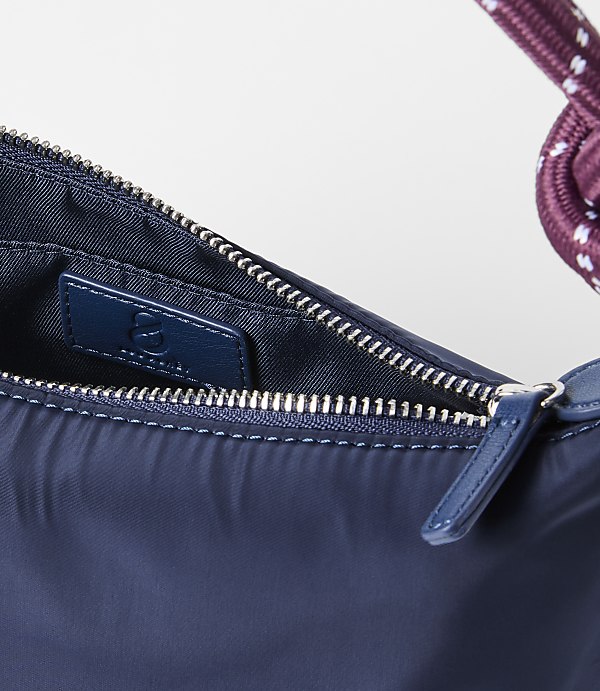 A close-up of a navy blue handbag with a braided strap is set against a plain white background.