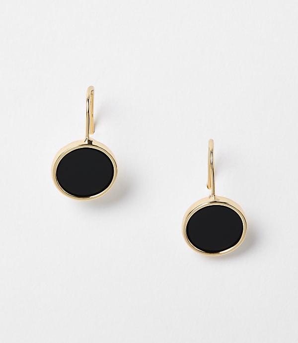 A pair of gold earrings with black circular stones hang against a plain white background.