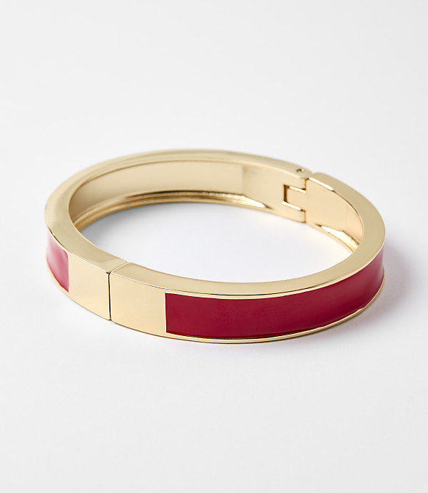 A gold bangle bracelet with red enamel accents rests on a plain white background.