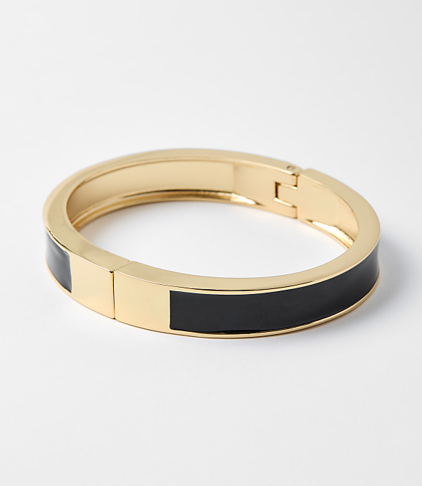 A gold bangle bracelet with black enamel accents rests on a plain white background.