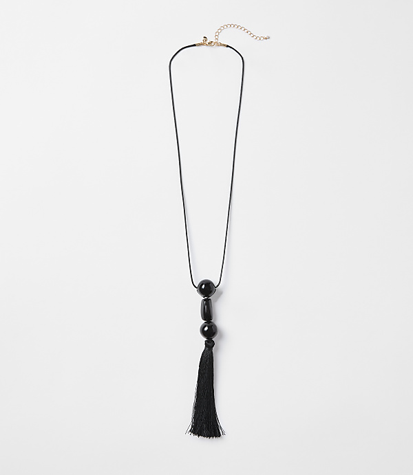 A black tassel necklace with three black beads hangs against a plain white background.