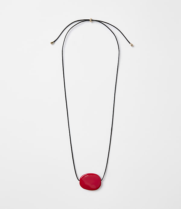 A simple black cord necklace with a single, smooth red stone pendant hangs against a plain white background.