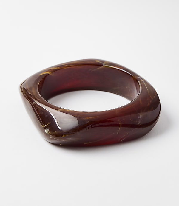 A chunky, translucent amber-colored bangle with swirling patterns rests on a plain white background.
