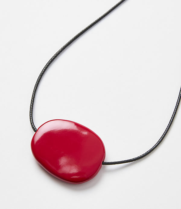 A glossy red, pebble-shaped pendant hangs from a thin black cord against a plain white background.