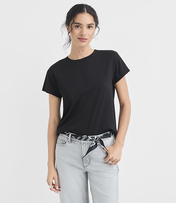 A woman in a black t-shirt and light-wash jeans stands against a plain white background.