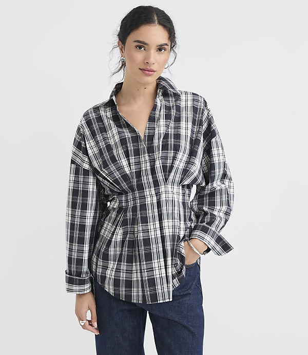 A woman in a plaid shirt and jeans stands against a plain white background.