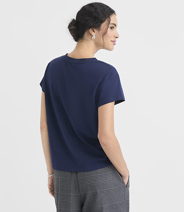 A woman in a navy t-shirt and plaid pants stands against a plain white background.