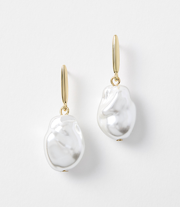 A pair of gold hoop earrings with irregular white pearls hang against a plain white background.