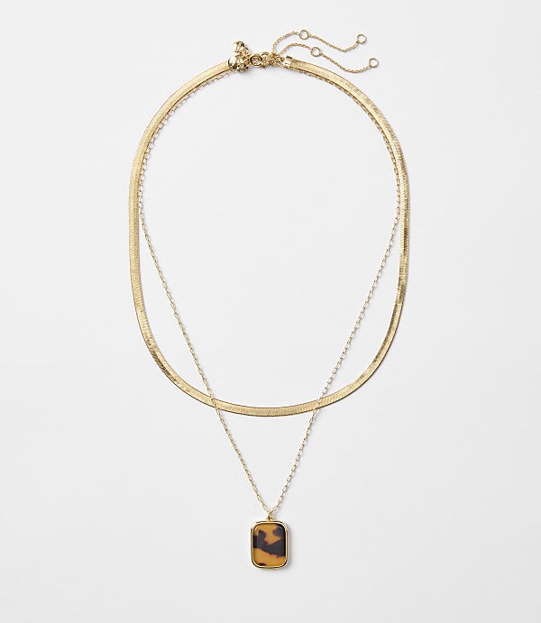 A layered gold necklace with a tortoise shell pendant hangs against a plain white background.