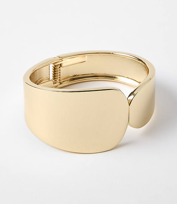 A polished gold cuff bracelet with a hinge closure rests on a plain white background.
