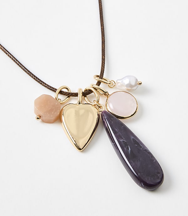A gold heart locket and various colorful gemstone charms hang from a brown cord against a plain white background.
