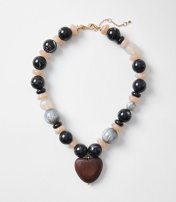A chunky necklace with a wooden heart pendant rests on a plain white background.