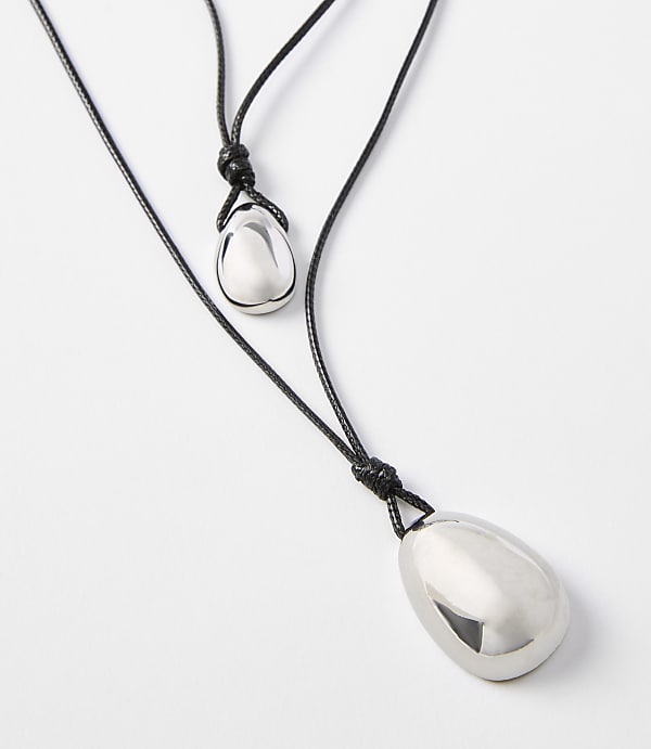 Two polished silver teardrop pendants hang from black cords against a plain white background.