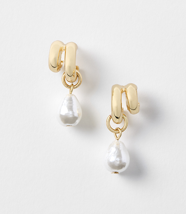 A pair of gold earrings with pearl drops hang against a plain white background.