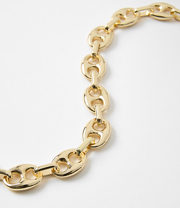 A close-up of a gold chain with oval links lies on a plain white background.