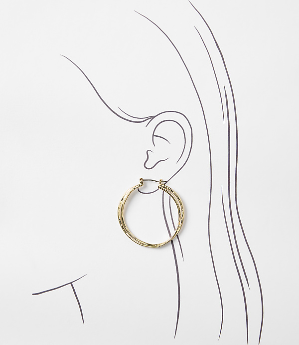 A textured gold hoop earring is displayed on a stylized drawing of a woman's ear and hair against a white background.