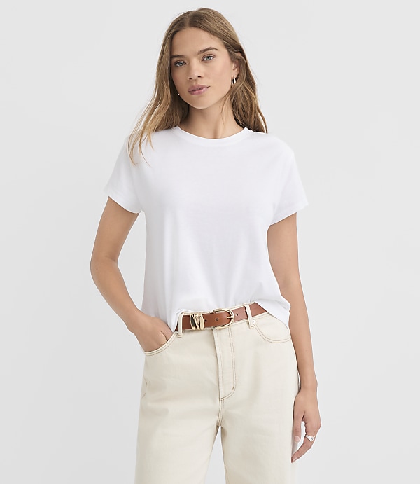 A woman in a white t-shirt and light-colored pants stands against a plain white background.