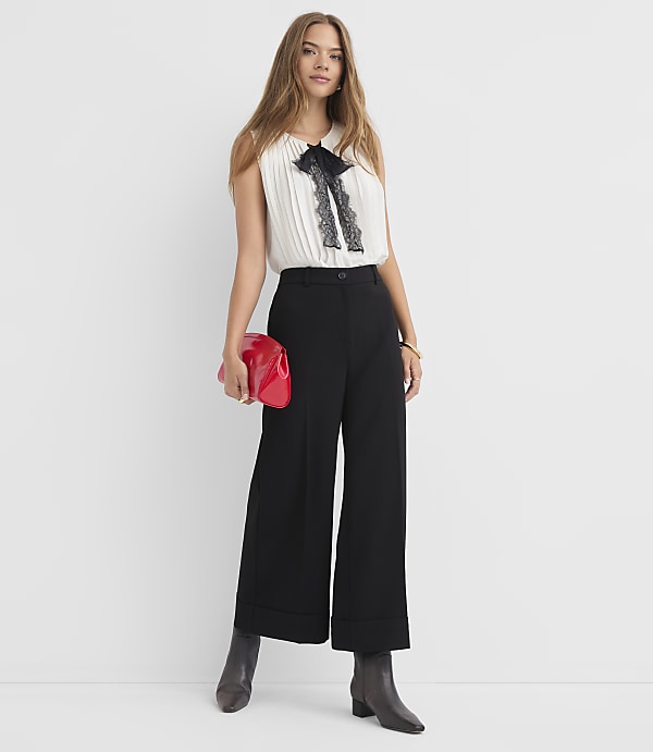 A woman in a white blouse and black pants holds a red clutch against a plain white background.
