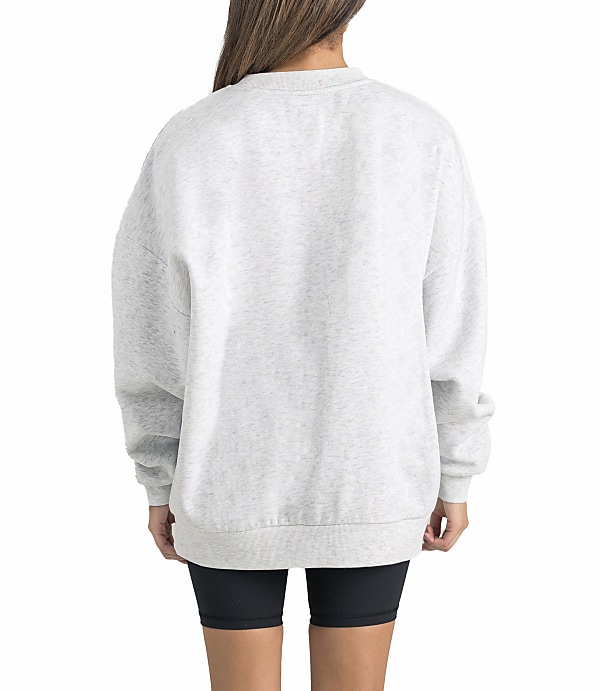 A person wearing a light gray sweatshirt and black shorts stands against a plain white background.