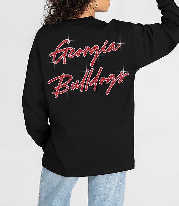 A person in a black long-sleeved shirt with "Georgia Bulldogs" in glittery red script on the back stands against a plain white background.