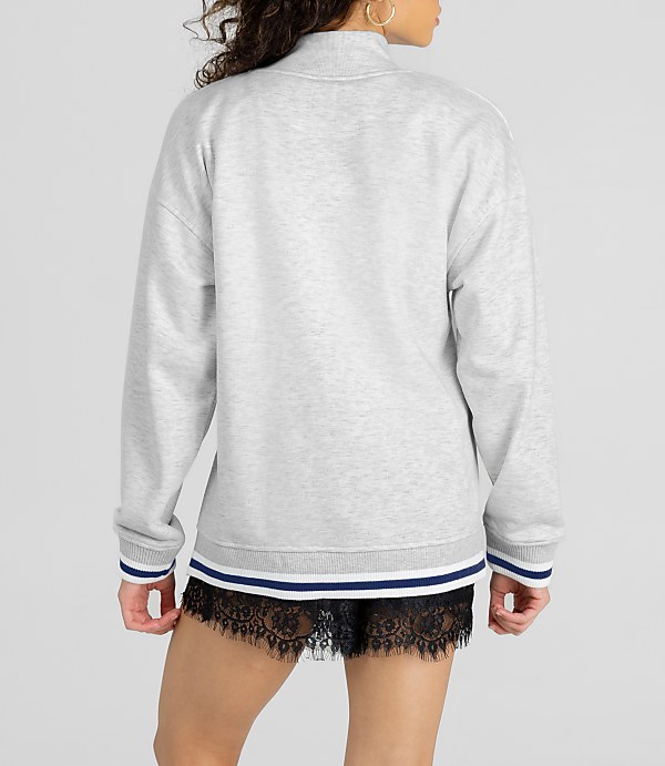 A woman in a grey sweatshirt and black lace shorts stands against a plain white background.