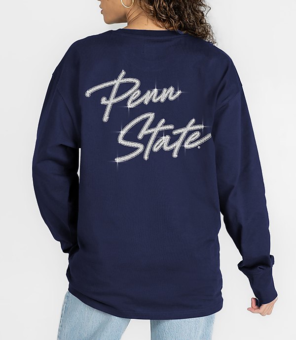 A person in a navy blue long-sleeved shirt with "Penn State" written in rhinestones stands against a plain white background.