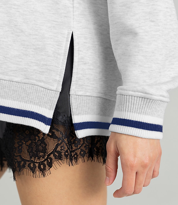 A close-up shot focuses on the hem of a light gray sweatshirt with navy and white striped cuffs, revealing black lace trim peeking out from underneath.
