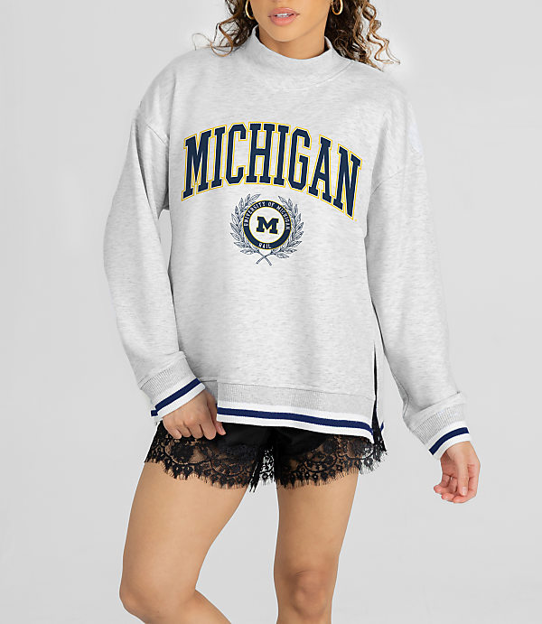 A woman in a gray "Michigan" sweatshirt and black lace shorts stands against a white background.